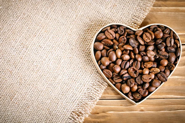 Fried coffee beans lie in the form of heart on wooden boards and burlap. — Stock Photo, Image