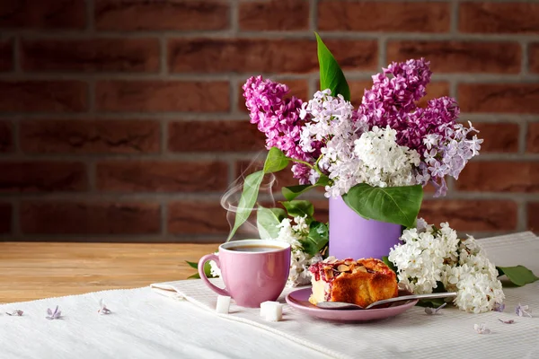 Stilleven met takken van lila en een kopje koffie op een houten tafel. — Stockfoto