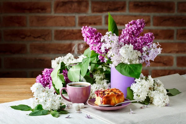 Bodegón con ramas de lila y una taza de café sobre una mesa de madera . — Foto de Stock