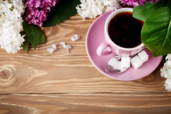 Bodegón con ramas de lila y una taza de café sobre una mesa de madera . — Foto de Stock