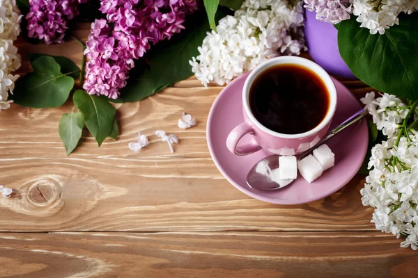 Bodegón con ramas de lila y una taza de café sobre una mesa de madera . — Foto de Stock