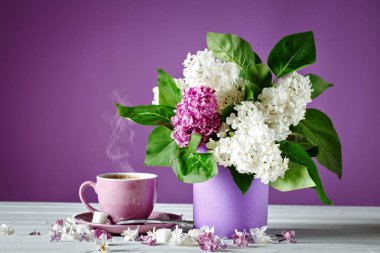 Natürmort leylak dalı ve bir fincan kahve ahşap bir masa üzerinde.