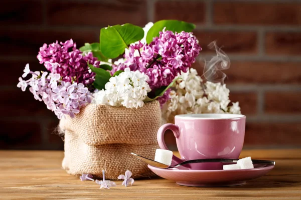 Bodegón con ramas de lila y una taza de café sobre una mesa de madera . —  Fotos de Stock