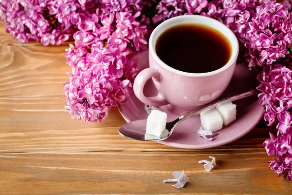 Natureza morta com ramos de lilás e uma xícara de café em uma mesa de madeira . — Fotografia de Stock