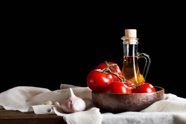 Domates, sarımsak ve zeytinyağı ahşap kurullarında natürmort. Siyah bir arka plan üzerinde.