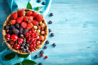 Mavi ahşap bir masa üzerinde bir hasır plaka olgun çilek.