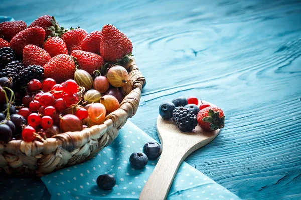 Ripe berries in a wicker plate on a blue wooden table. Royalty Free Stock Images
