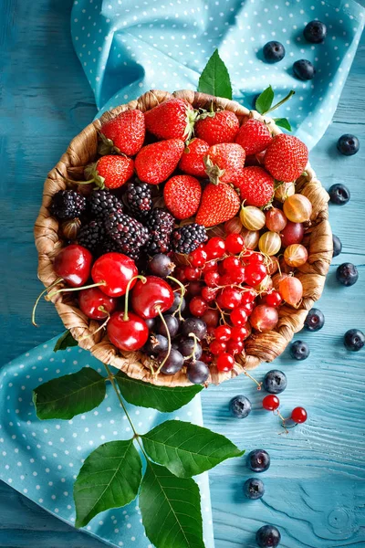 Ripe berries in a wicker plate on a blue wooden table. Royalty Free Stock Images