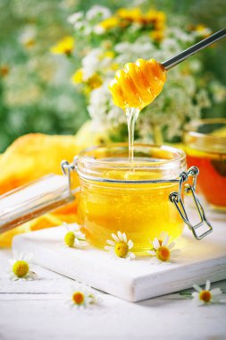 Tasty and healthy honey on white wooden table with flowers of chamomile. clipart