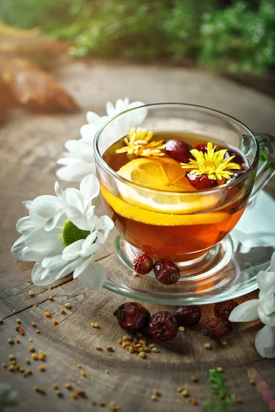 Eine gesunde Tasse Tee mit Zitrone und Hagebutten und Blumen auf einem Holztisch. Selektiver Fokus. — Stockfoto