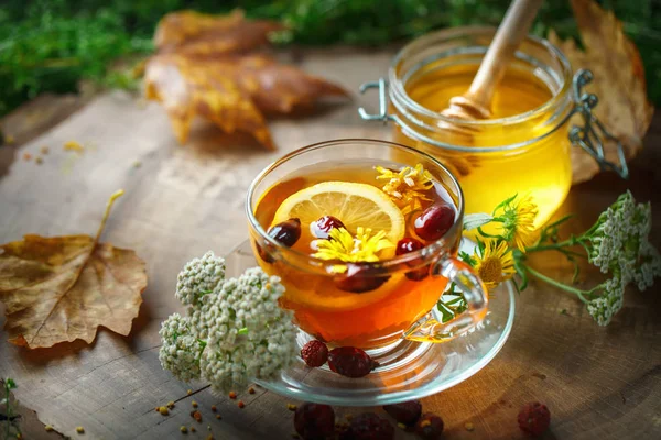 Köstlichen frischen Honig und eine Tasse gesunden Tee mit Zitrone und Hagebutten auf einem Holztisch. Selektiver Fokus. — Stockfoto