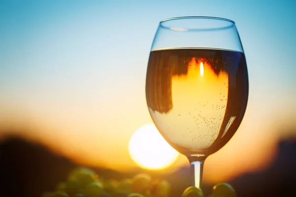 Skleničku bílého vína při západu slunce, s odrazem domů. — Stock fotografie