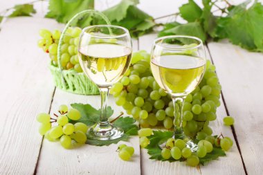 Gözlük beyaz şarap ve ahşap bir masa üzerinde taze üzüm ile.