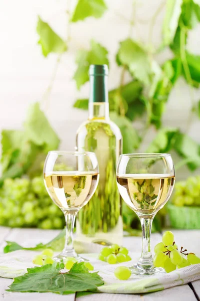 Copos com vinho branco, uvas frescas e uma garrafa de vinho branco numa mesa de madeira . — Fotografia de Stock