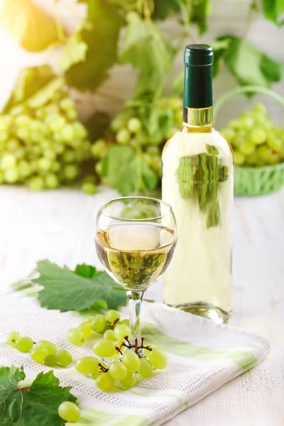 Ein Glas Weißwein, frische Trauben und eine Flasche Weißwein auf einem Holztisch. — Stockfoto