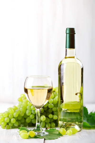Sklenice na bílé víno, čerstvé vinné hrozny a láhev bílého vína na dřevěný stůl. — Stock fotografie
