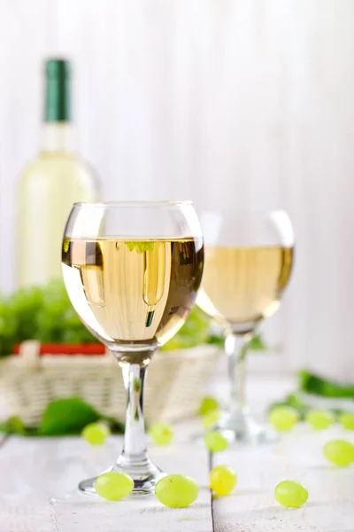 Gläser mit Weißwein, frischen Trauben und einer Flasche Weißwein auf einem Holztisch. — Stockfoto