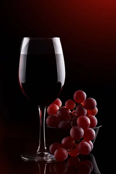 Ein Glas Rotwein und rote Trauben auf dunklem Hintergrund. — Stockfoto