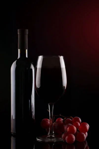 Flasche Rotwein, ein Glas Rotwein und Trauben auf dunklem Hintergrund. — Stockfoto