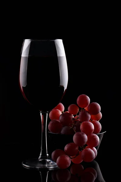 Ein Glas Rotwein und rote Trauben auf schwarzem Hintergrund. — Stockfoto
