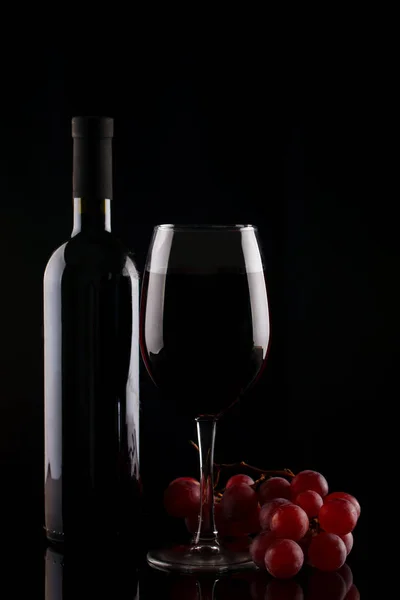 Flasche Rotwein, ein Glas Rotwein und Trauben auf schwarzem Hintergrund. — Stockfoto