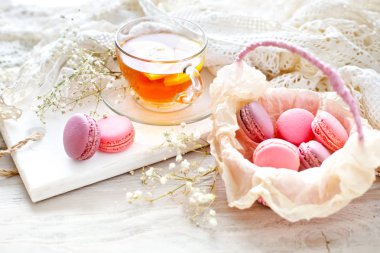 Çay limon, kır çiçekleri ve beyaz tahta masada macaron.