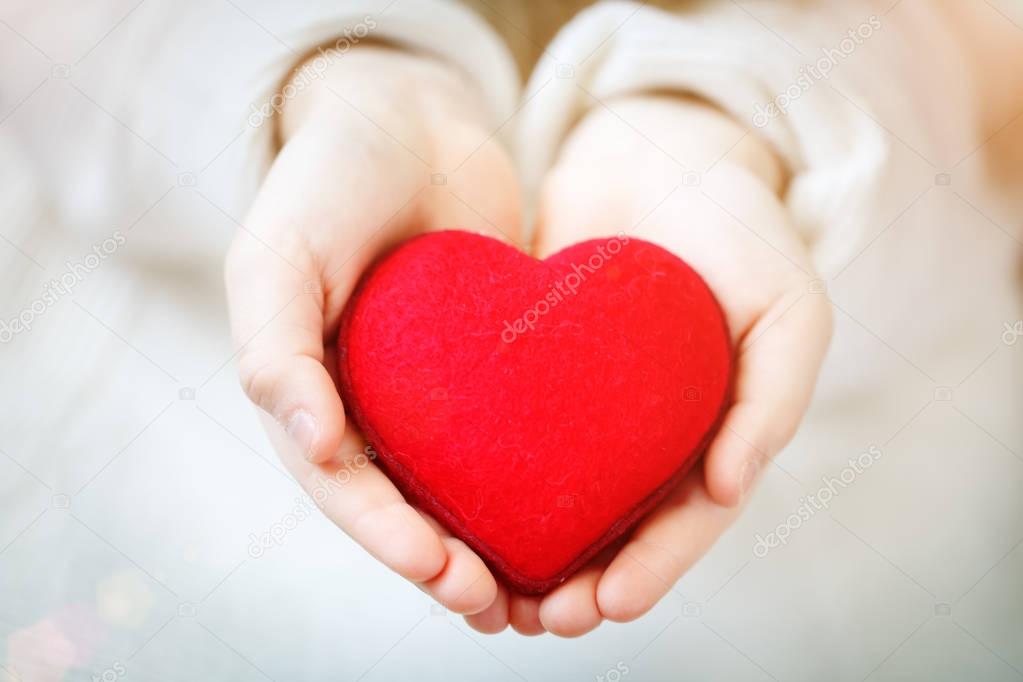 Red heart in hands of the little girl. Symbol of love and family.Valentines day card. Mothers day. Backgrounds for social posters. Selective focus.