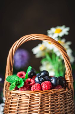 Ahududu ve yaban mersini bir sepetin içinde papatya çayı ve koyu arkaplanda yapraklar. Yaz ve sağlıklı gıda konsepti. Seçici odaklanma. Kopyalama alanı olan arkaplan.