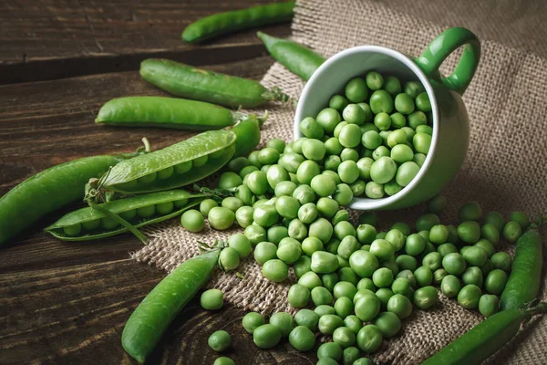 Deliciosos guisantes verdes maduros tumbados sobre una mesa de madera. — Foto de Stock