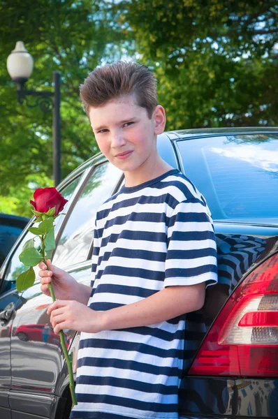 El chico sostiene una rosa cerca del coche. el concepto de amor —  Fotos de Stock