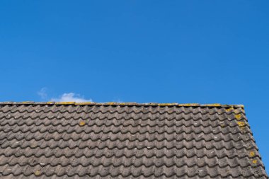 Gri çatılı çatı kiremitleri ve güneşli bir günde bulutlu açık mavi bir gökyüzü.