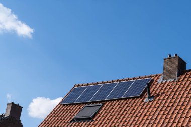 Kırmızı kiremitli çatı, baca ve güneş panelleri yenilenebilir enerji ve açık mavi gökyüzü oluşturmak için.