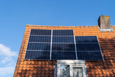 Kırmızı çatı kiremitleri ve yenilenebilir enerji üretmek için güneş panelleri ve açık mavi gökyüzü