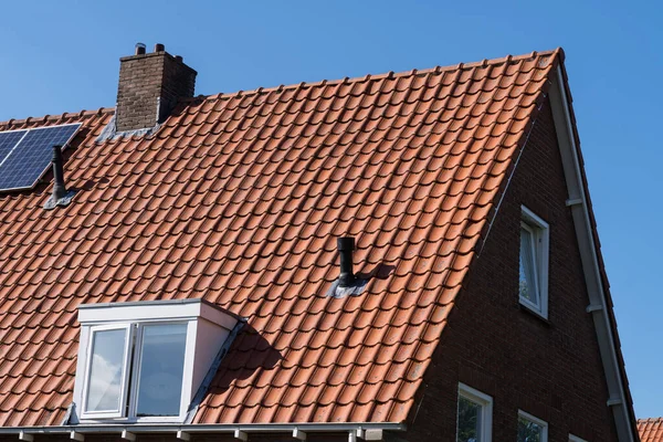 Roof with red roof tiles, chimney and solar panels for making renewable energy and a clear blue sky