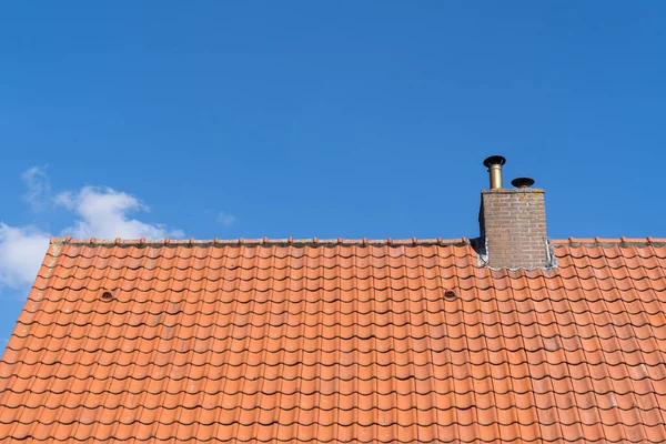 Roof with red roof tiles and chimney and a clear blue sky with some clouds on a sunny day