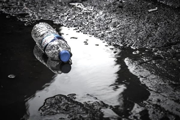 Plastikflasche mit Wasser auf einer Pfütze auf der Straße — Stockfoto