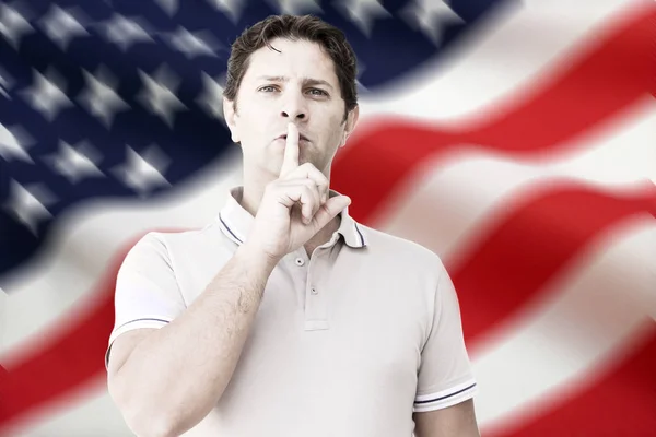 Mann zeigt stummes Zeichen und hält den Zeigefinger vor den Lippen gegen eine amerikanische Flagge im Hintergrund — Stockfoto