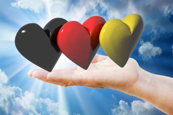 Rękę trzymając trzy serca z kolory flagi niemieckiej — Zdjęcie stockowe