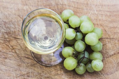 Bir bardak İtalyan beyaz şarap, ahşap bir tepsi üzerinde duruyor, bazı beyaz üzüm yakın