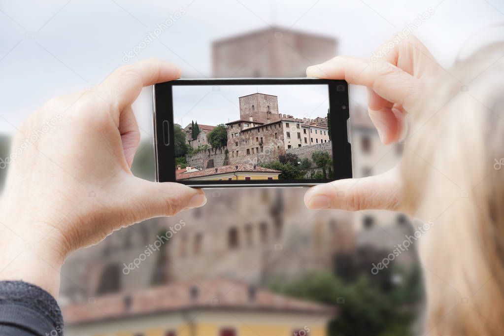 A woman is going to shoot the photo of a castle using a smartphone