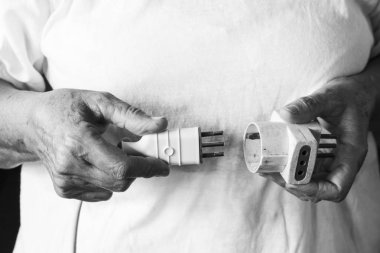 Yaşlı bir kadın elinde iki elektrik fiş bir diğerine bağlanan