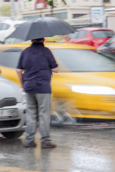 El hombre se detiene en la calle sosteniendo un paraguas negro mientras los coches pasan por todas partes — Foto de Stock