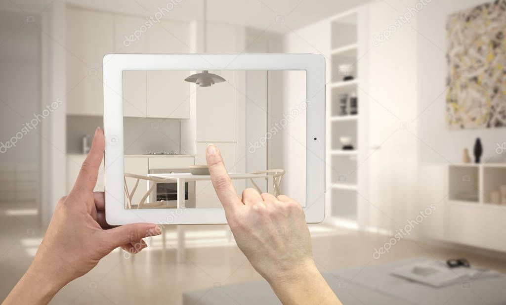 Hands holding and pointing on tablet showing modern kitchen. Blurry minimalist white kitchen in the background, architecture interior design presentation