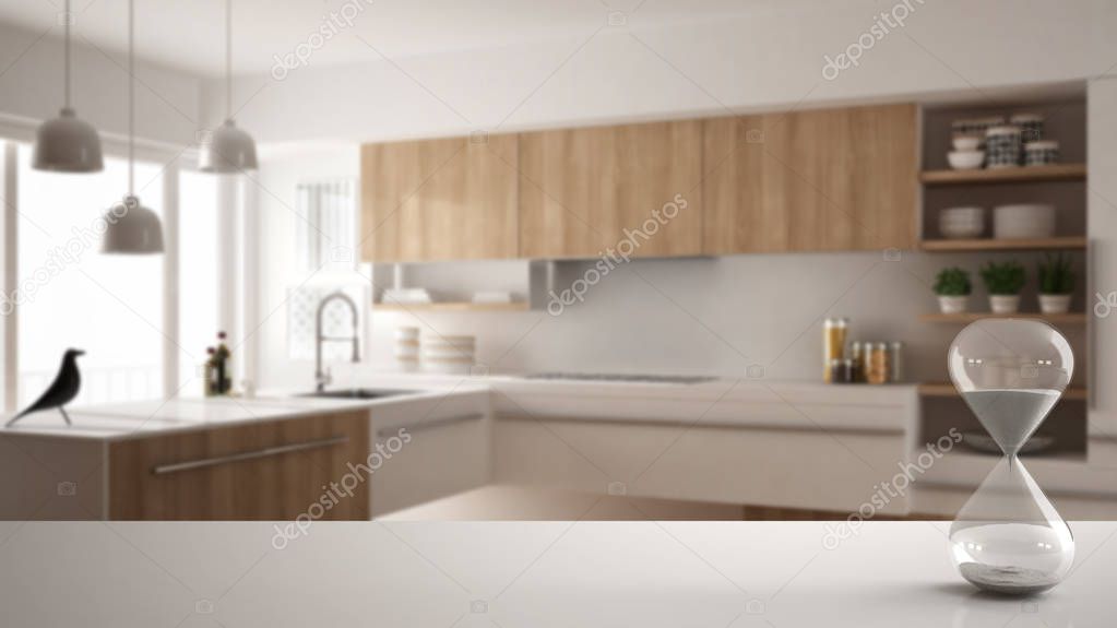 White table or shelf with crystal hourglass measuring the passing time over blurred modern kitchen with parquet floor, architecture interior design background