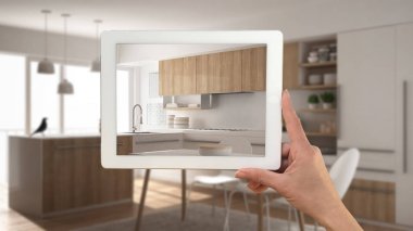 Gerçek gösterilen tablet tutan el minimalist beyaz ve ahşap Mutfak bitmiş. Mimari iç tasarım sunum arka planda modern bulanık mutfak