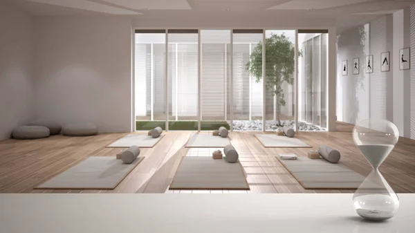 Mesa blanca o estante con reloj de arena de cristal que mide el tiempo que pasa sobre el estudio de yoga con esteras y accesorios, meditación, diseño de interiores de arquitectura, espacio de copia de fondo —  Fotos de Stock