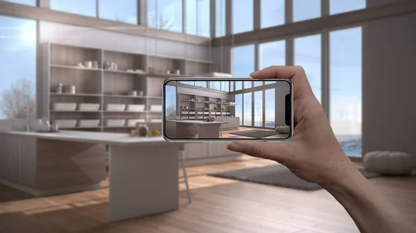 Hand holding smart phone, AR application, simulate furniture and interior design products in real home, architect designer concept, blur background, modern white and wooden kitchen