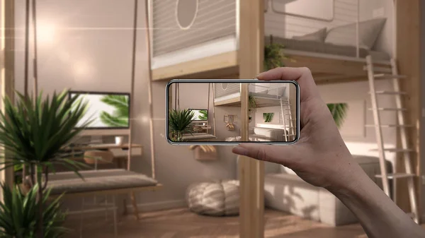 Hand holding smart phone, AR application, simulate furniture and interior design products in real home, architect designer concept, studio apartment with loft bunk double bed, swing