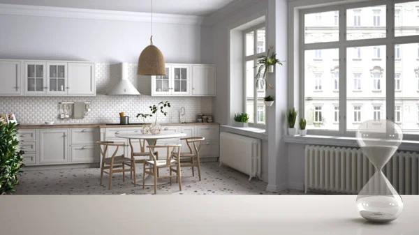 White table or shelf with crystal hourglass measuring the passing time over minimalist classic kitchen with table and chairs, architecture interior design, copy space background