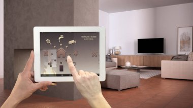 Dijital tablette akıllı uzaktan kumanda sistemi. Uygulama simgeleri olan aygıt. Oturma odası beton şömine, kanepe ve fonda puf, mimari iç tasarım.
